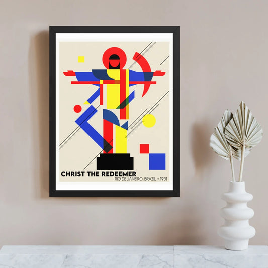 Bauhaus Christ the Redeemer wall art in a black frame, with the Rio de Janeiro statue abstracted into red, yellow, blue and black geometric shapes, with outstretched arms and scattered circles and squares.