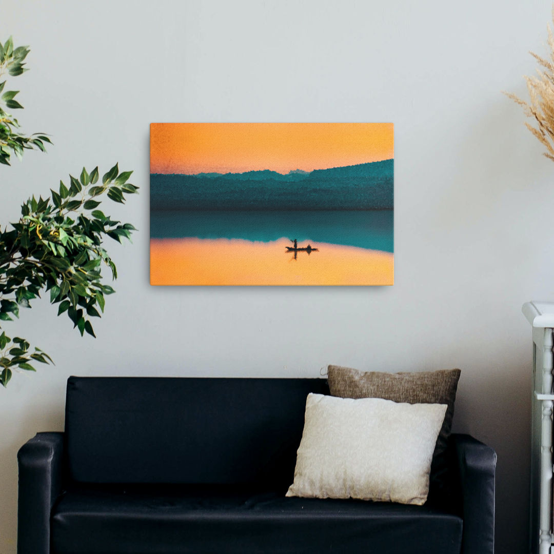 Mockup image of the artwork "Serenity on the Horizon Canvas Print" depicting a stunning sunset over the mountains, reflecting in the tranquil lake. A silhouette of a sailing boat adds an elegant touch to the composition.