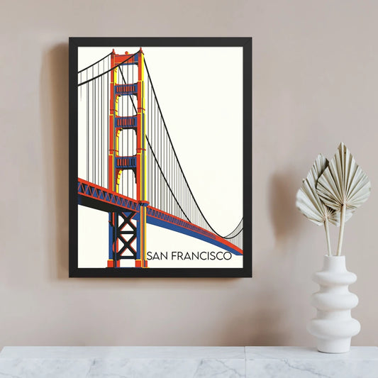 Bauhaus Golden Gate Bridge print in a black frame, showing the San Francisco suspension bridge’s red-orange towers and cables with blue and yellow structural details on a clean cream background.