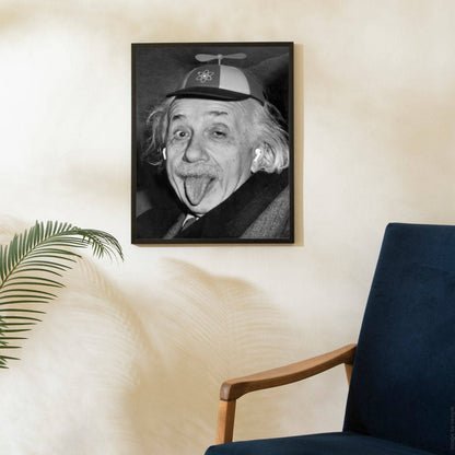 Black and white portrait photograph of Albert Einstein sticking his tongue out, wearing a propeller hat decorated with an atom symbol, vintage poster print