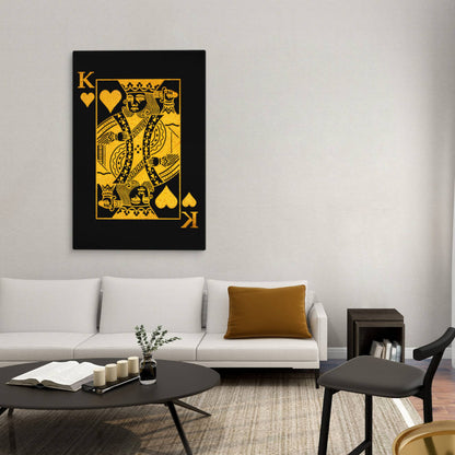 A cozy, modern living room with a black and gold king of hearts canvas print as the statement piece on a neutral-toned wall, paired with a light sofa and warm accent pillows, balancing bold art with a soft, inviting atmosphere.
