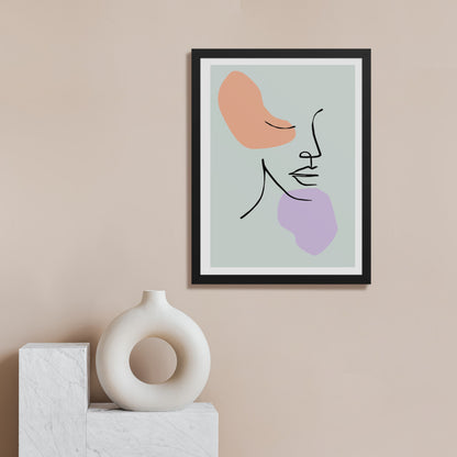 A contemporary interior with a beige wall displaying the same black framed abstract line art print containing peach and lavender shapes with curved lines. On a surface below sits a white circular sculptural vase or decorative object with a hollow center.